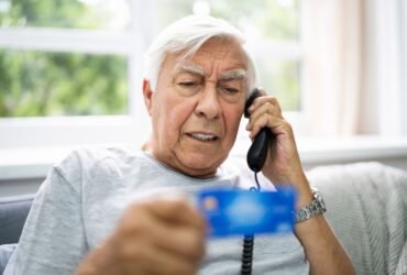 Old man reading credit card information on the phone